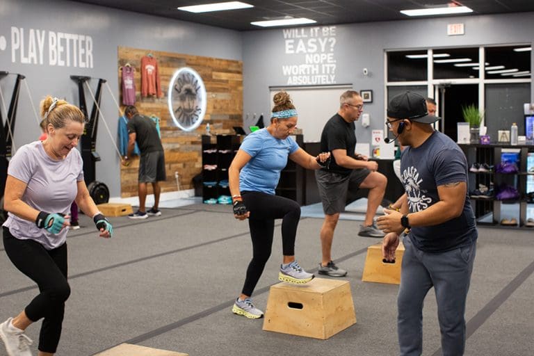Group personal training class, members working out at Coastal Fitness doing a box step-up